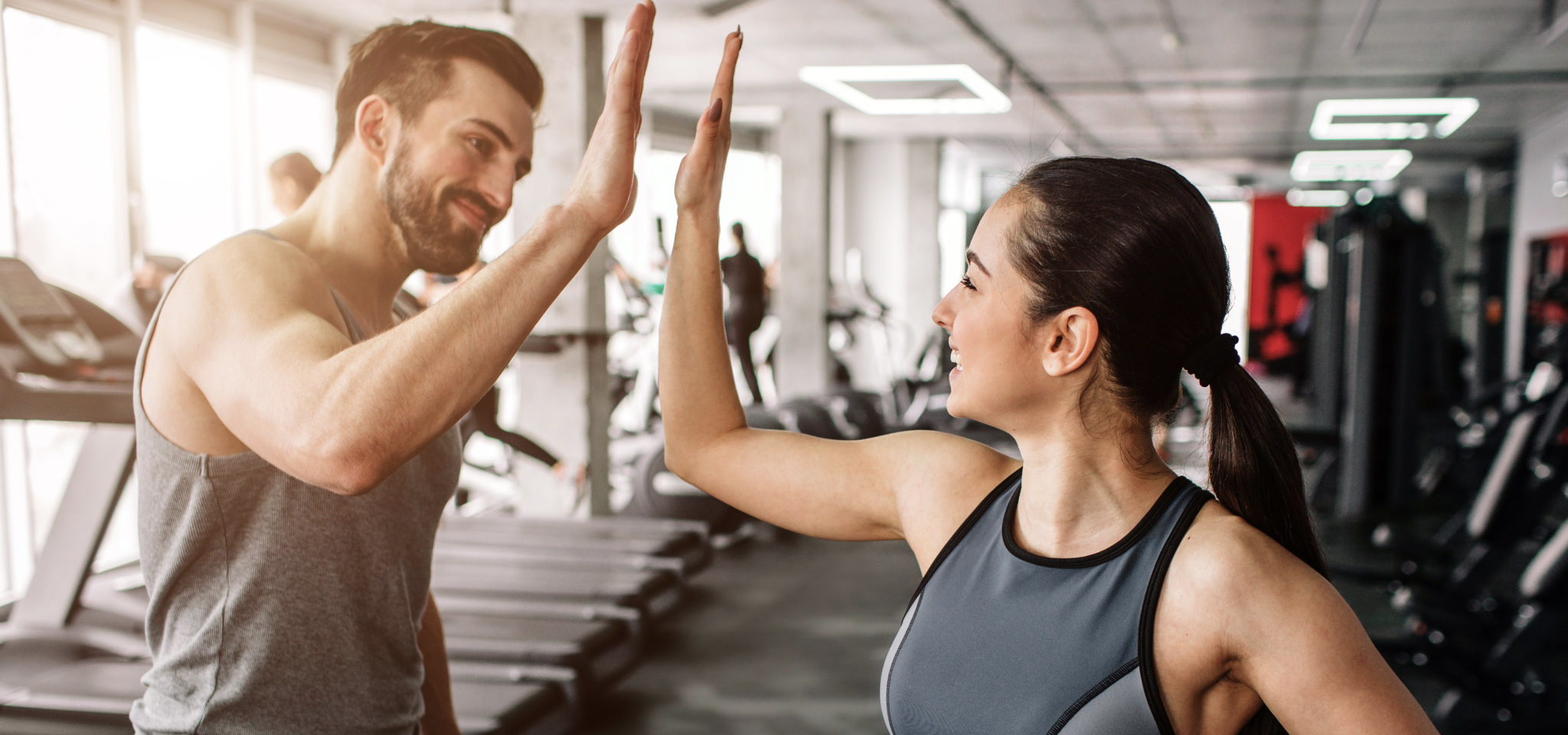 A beautiful girl and her well-built boyfriend are greeting each other with a high-five. They are happy to see each othr in the gym. Young people are ready to start their workout.