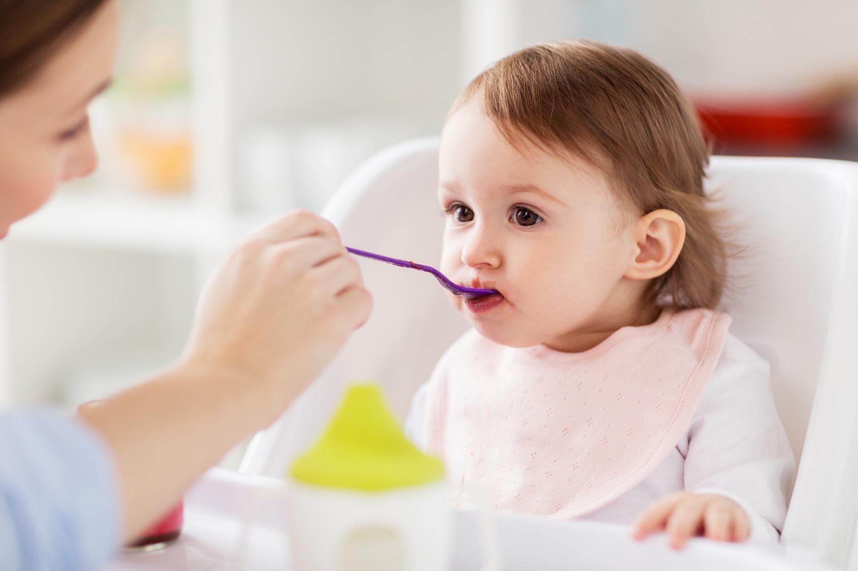 happy mother feeding baby with puree at home